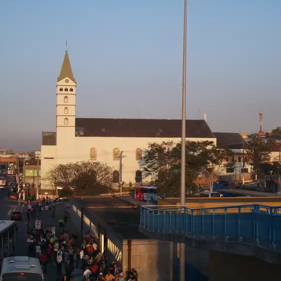 Pessoas na passarela de Guaianases no fim de tarde, com a igreja ao fundo
